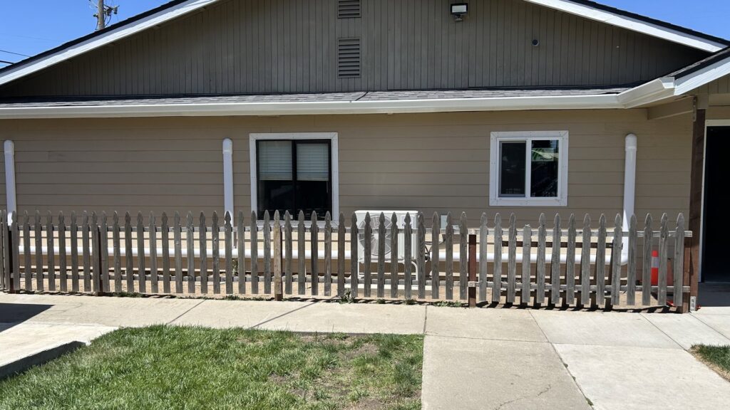 An outdoor HVAC condenser unit situated behind a small wooden fence, installed by Service Kings Heating and Air in Jamestown, ND.