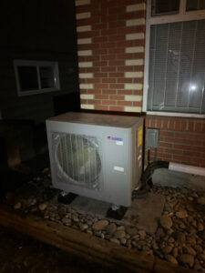 An outdoor GREE HVAC unit installed next to a brick building by Comfitrust in Boston, MA