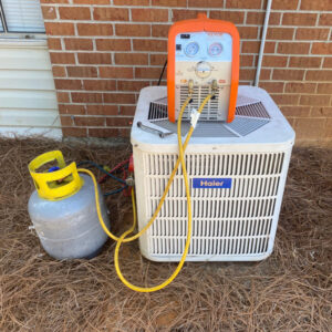 An outdoor HVAC unit with a refrigerant tank and manifold gauges connected, indicating service by Eleven Heating and Cooling in Birmingham, AL.