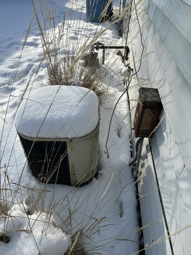 An outdoor HVAC condenser unit covered in snow, serviced by Handy Properties LLC in Akron, OH.