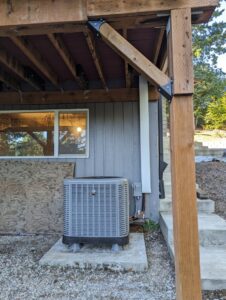 An outdoor HVAC unit installed neatly under a deck by Gresham Heating and Air Conditioning in Wood Village, OR.
