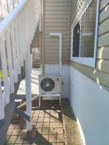 An outdoor GREE HVAC unit installed on a stand under a staircase by Comfitrust in Boston, MA