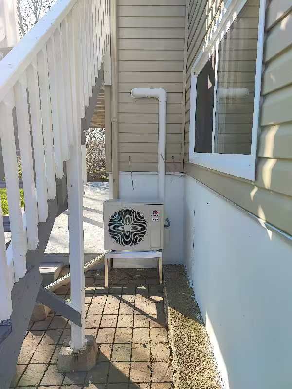 An outdoor GREE HVAC unit installed on a stand under a staircase by Comfitrust in Boston, MA