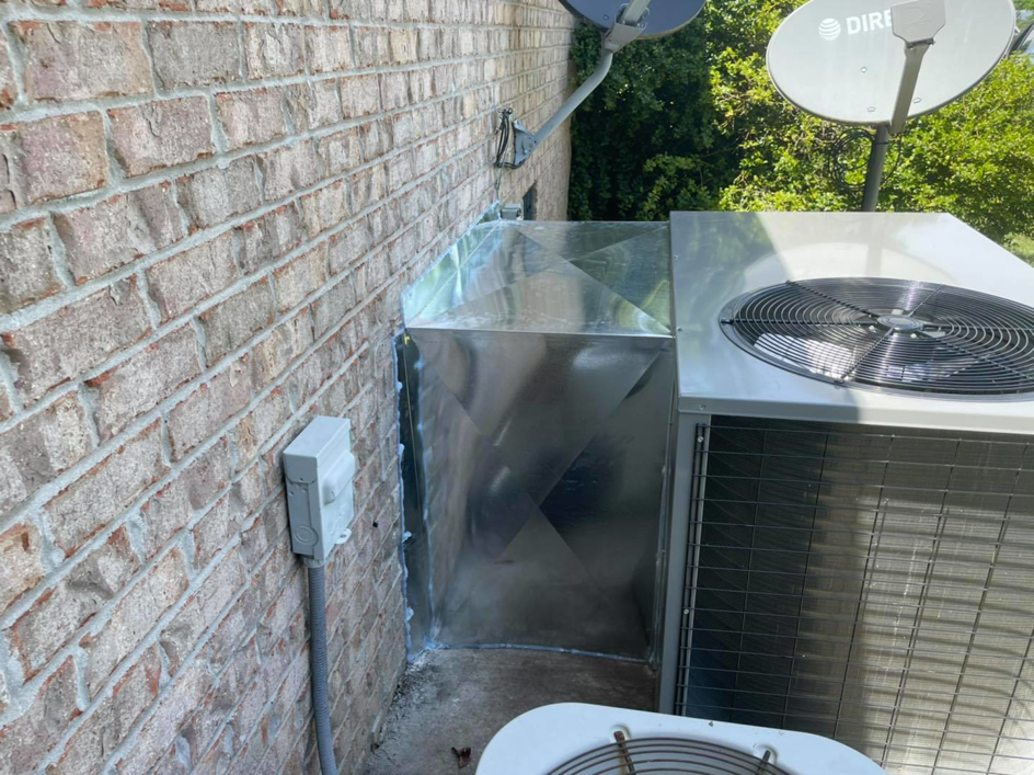 An outdoor HVAC unit connected to new metal ductwork against a brick wall by Wright Air Care in Murfreesboro, TN.