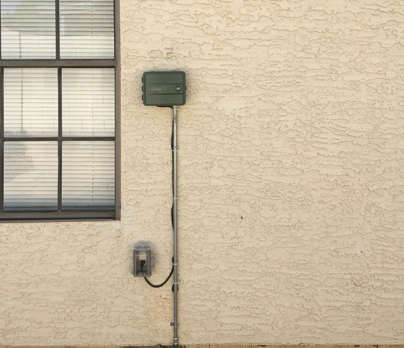 Outdoor irrigation controller and electrical wiring installation on a stucco wall by Earth Electric in Mesa, AZ