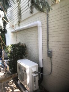 An outdoor mini-split condenser unit with refrigerant lines installed on the side of a house by Chad Byers - Edge Guys Heating & Cooling in Carmel, IN