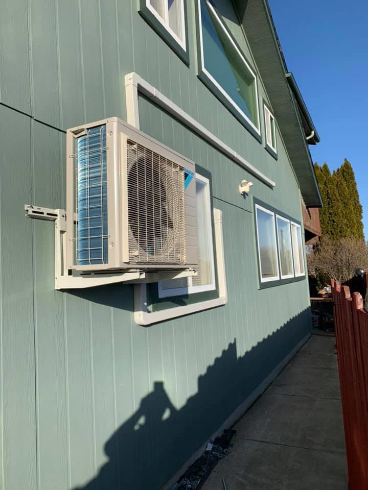 An outdoor mini-split condenser unit mounted on the side of a house by Finney Heating and Cooling LLC in Post Falls, ID.