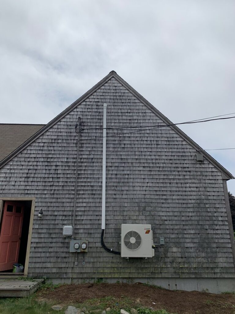 An outdoor mini-split condenser unit installed on a house by Atmos HVAC in Quincy, MA.