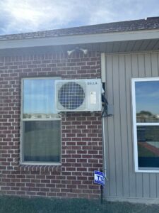 An outdoor mini-split condenser unit mounted on a brick wall by Budget Heating and Air in Mobile, AL.