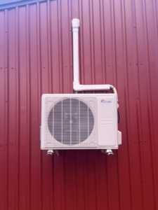 An outdoor mini-split condenser unit professionally installed on a red corrugated wall by HD Precision Works in Iota, LA.
