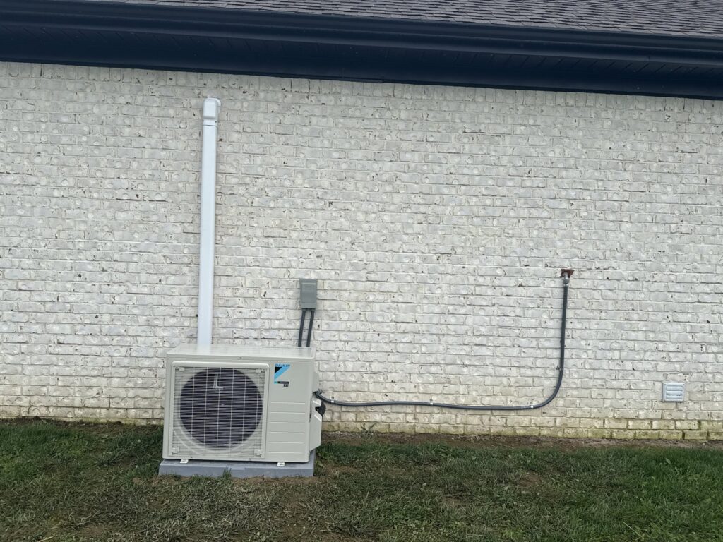 An outdoor mini-split condenser unit installed next to a white brick wall by Bama Air Systems in Cullman, AL.