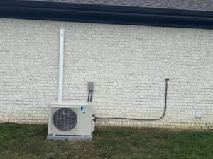 An outdoor mini-split condenser unit installed next to a white brick wall by Bama Air Systems in Cullman, AL.