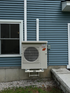 An outdoor mini-split condenser unit installed on a blue house by Infinity Heating and Cooling in Las Vegas, NV.