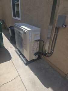 An outdoor mini-split condenser unit newly installed next to a residential building by Peace & Comfort Heating and Air in San Diego, CA.