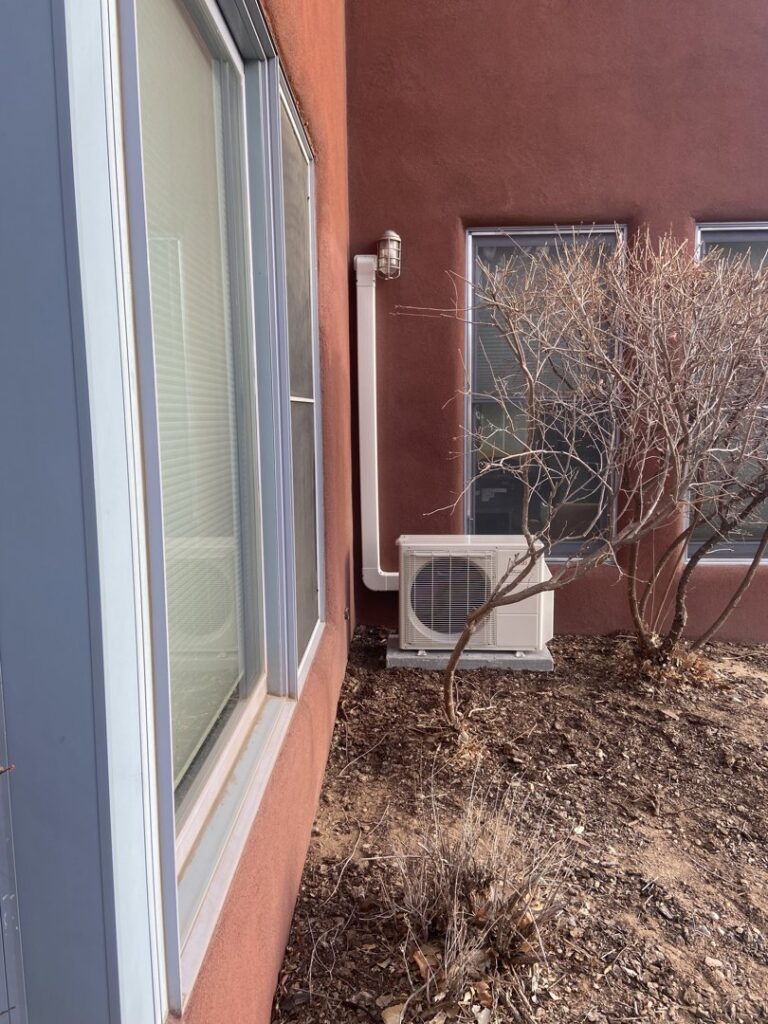 An outdoor mini-split condenser unit installed next to a building by Santa Fe Heating & Cooling LLC in Santa Fe, NM.