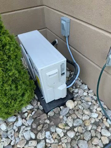 An outdoor mini-split condenser unit installed next to a residential home by Aire Serv of Rochester, NY