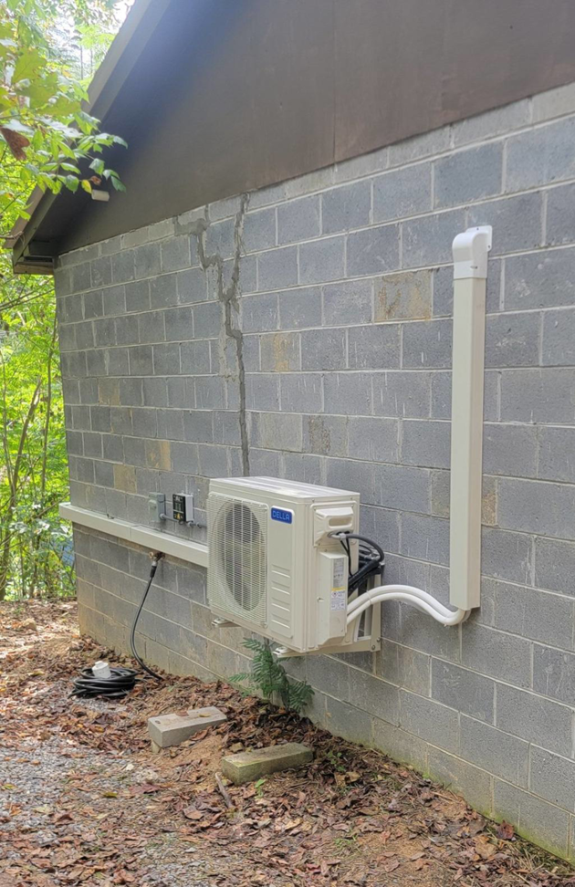 An outdoor mini-split HVAC unit professionally installed on a cinder block wall by Smoky Mountain Ducts & Vents in New Market, TN.