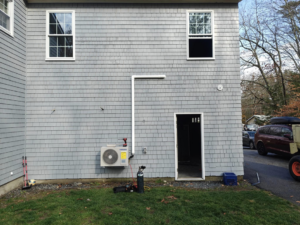 An outdoor mini-split HVAC unit being installed on the side of a house by Sutton HVAC in Suncook, NH.