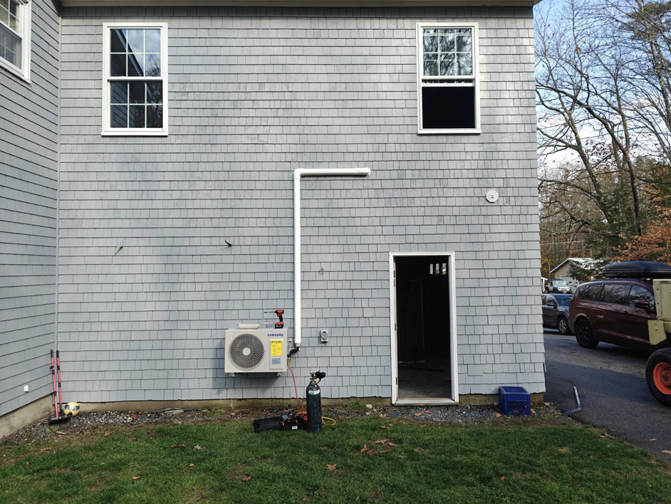 An outdoor mini-split HVAC unit being installed on the side of a house by Sutton HVAC in Suncook, NH.