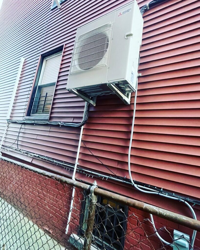 An outdoor mini-split or heat pump unit professionally installed on the side of a residential building by Deboque Duct Design Corp. in Staten Island, NY