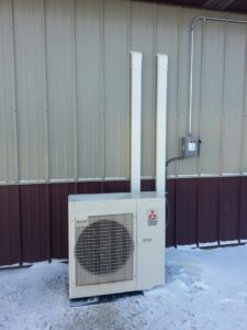 An outdoor Mitsubishi mini-split heat pump unit installed in the snow by Custom Climates in Iowa City, IA.