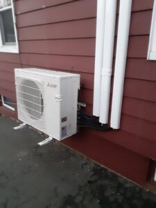 An outdoor Mitsubishi mini-split unit installed on a red-sided house by Climate Care Heating & Air Conditioning in Norwalk, CT