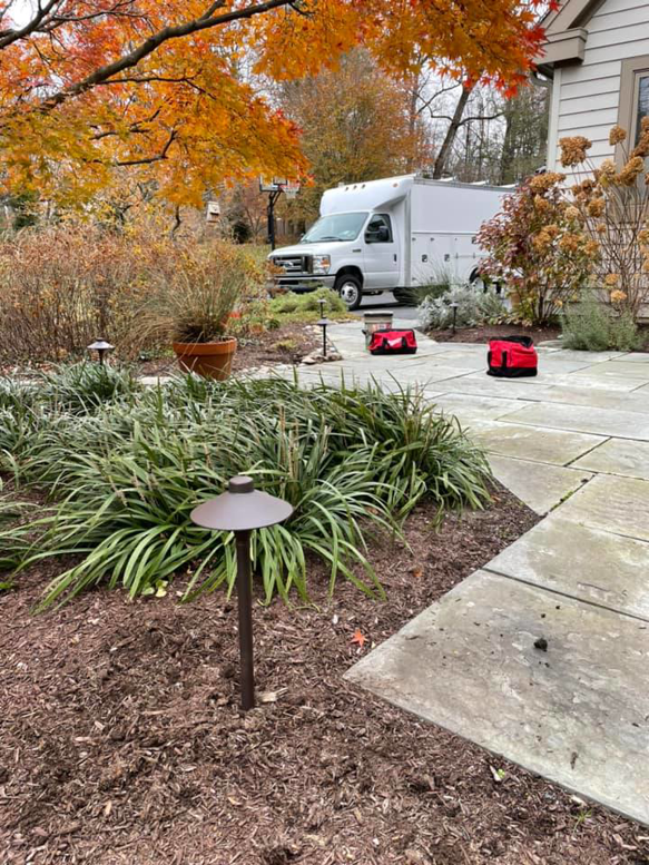 An outdoor path lighting installation site with a service truck and tool bags from K E Troutman Electrical Contractor in Newark, DE.