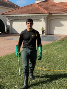 A Pro Care Lawn and Pest technician performing outdoor pest control service with a spray wand in Jacksonville, FL.