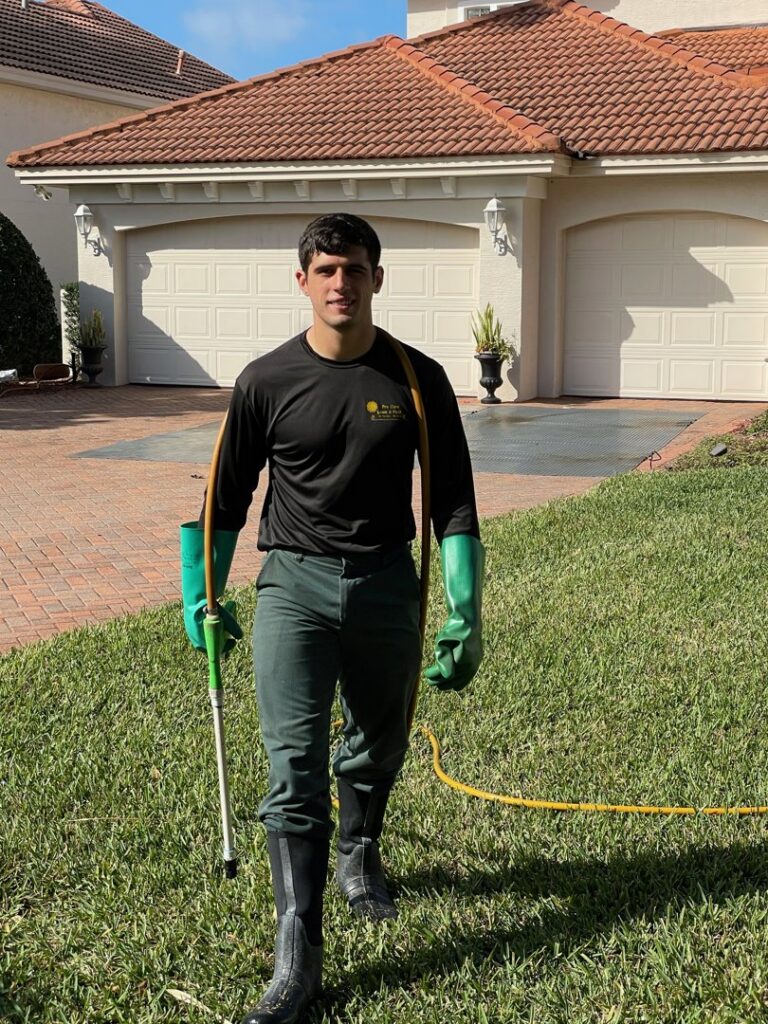 A Pro Care Lawn and Pest technician performing outdoor pest control service with a spray wand in Jacksonville, FL.