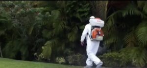 An Ideal Pest Control Inc technician in a hazmat suit performing outdoor pest control treatment in Miami, FL.
