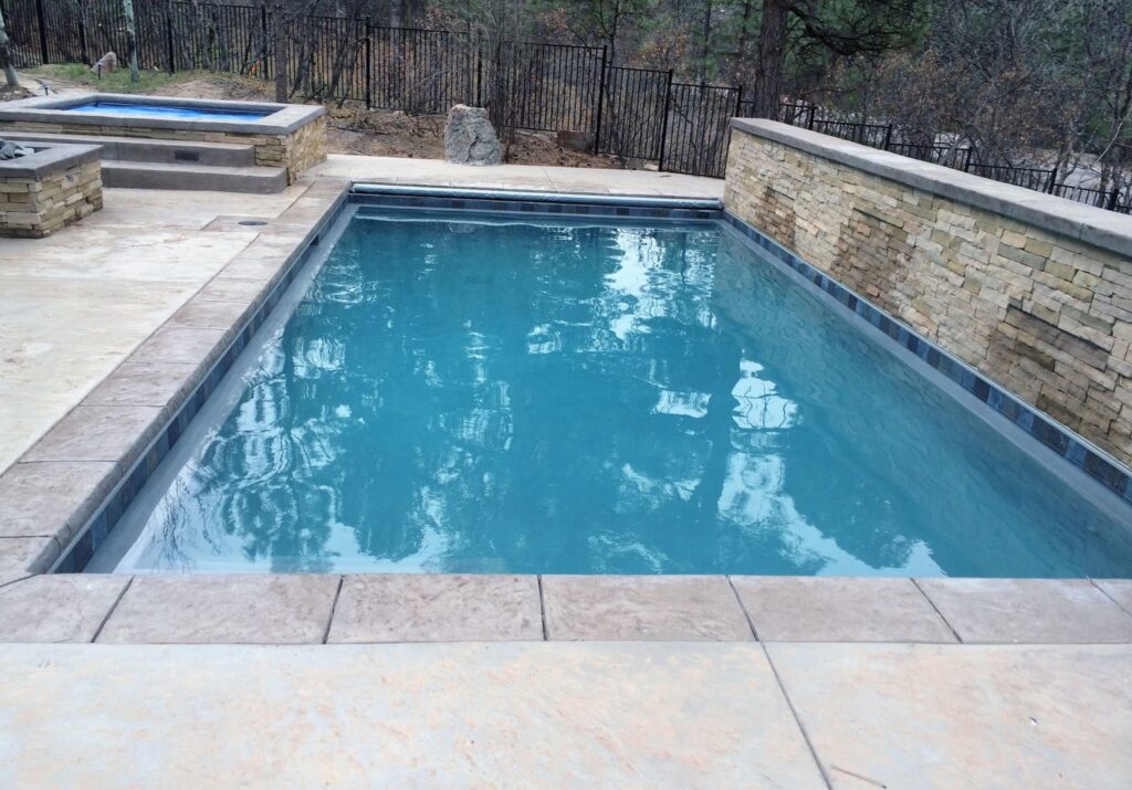 A newly completed outdoor pool with a raised spa and decorative stone wall by Wetworks Pool and Spa in Englewood, CO.
