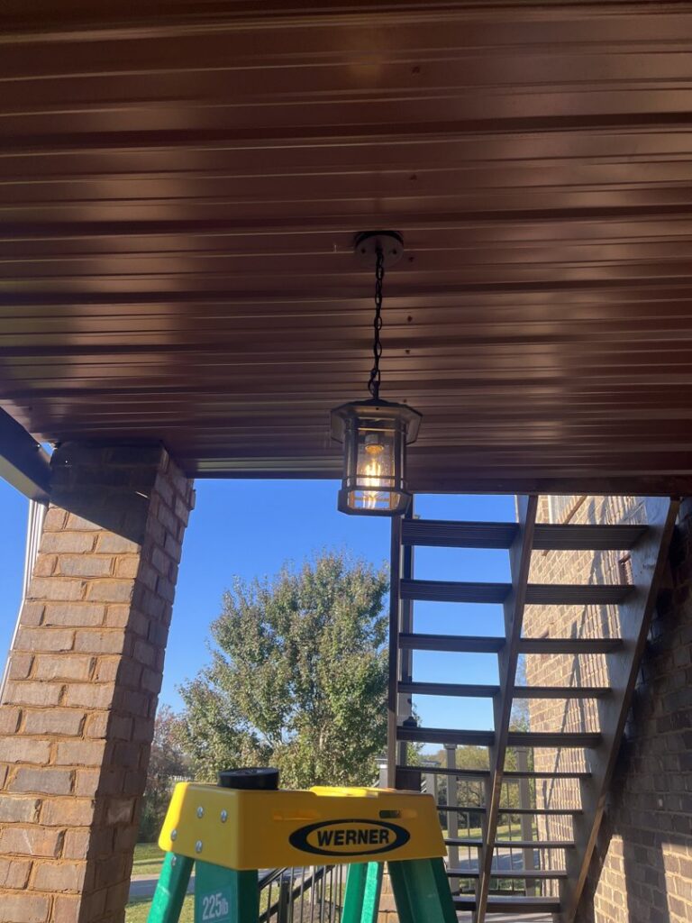 An outdoor hanging light fixture installed on a porch ceiling, with a ladder nearby, by Shocking Solutions in Knoxville, TN.
