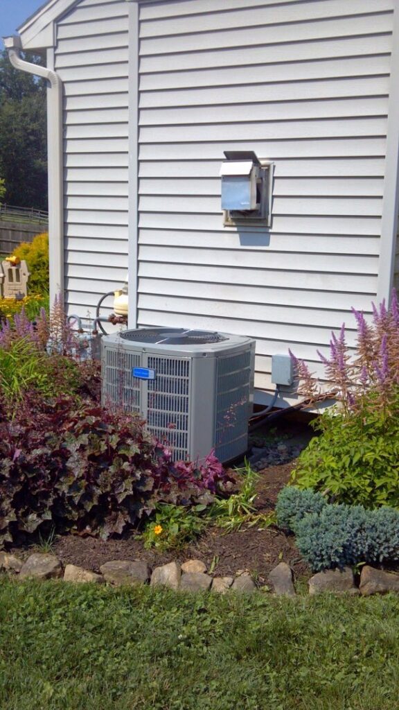 An outdoor residential air conditioning unit surrounded by landscaping, installed by Capitol Heating and Air in Morgantown, PA.