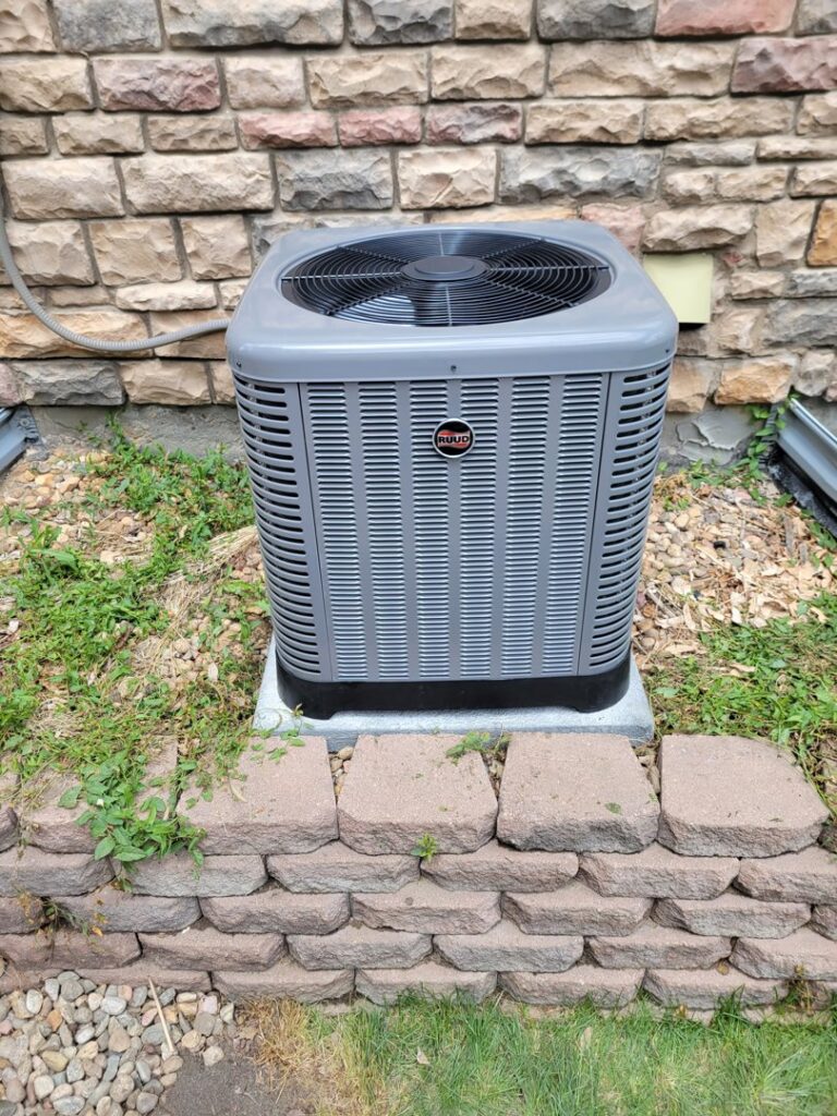 An outdoor residential AC unit next to a stone wall, serviced by Kraemer Mechanical in Broomfield, CO.