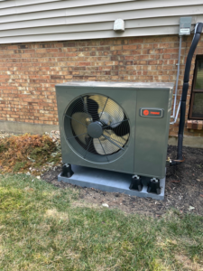 An outdoor Trane heat pump or AC condenser unit installed next to a brick building by Tri County Heating and Cooling in Longmont, CO.