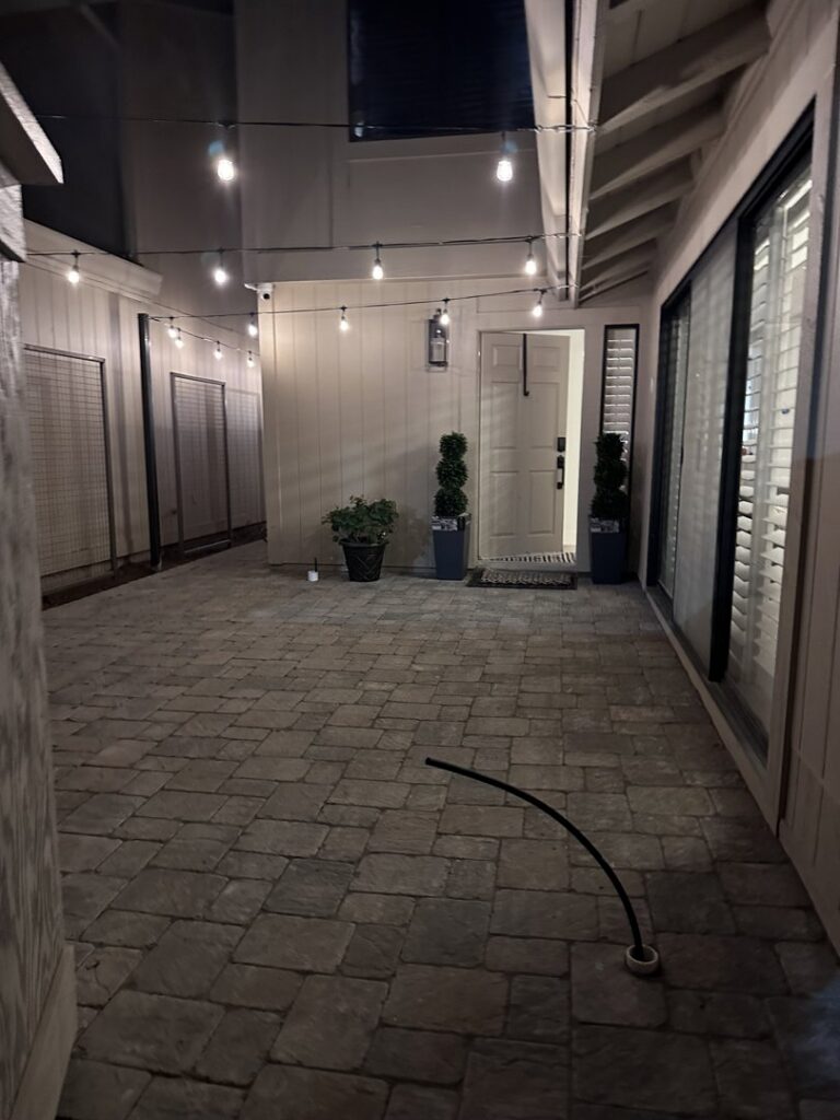 An outdoor walkway and patio illuminated with string lights and a wall sconce by The Lighting Geek in Sacramento, CA.