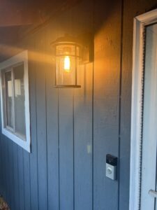 An outdoor wall light fixture installed and illuminated next to a door by Andrew's Electric in Kent, WA