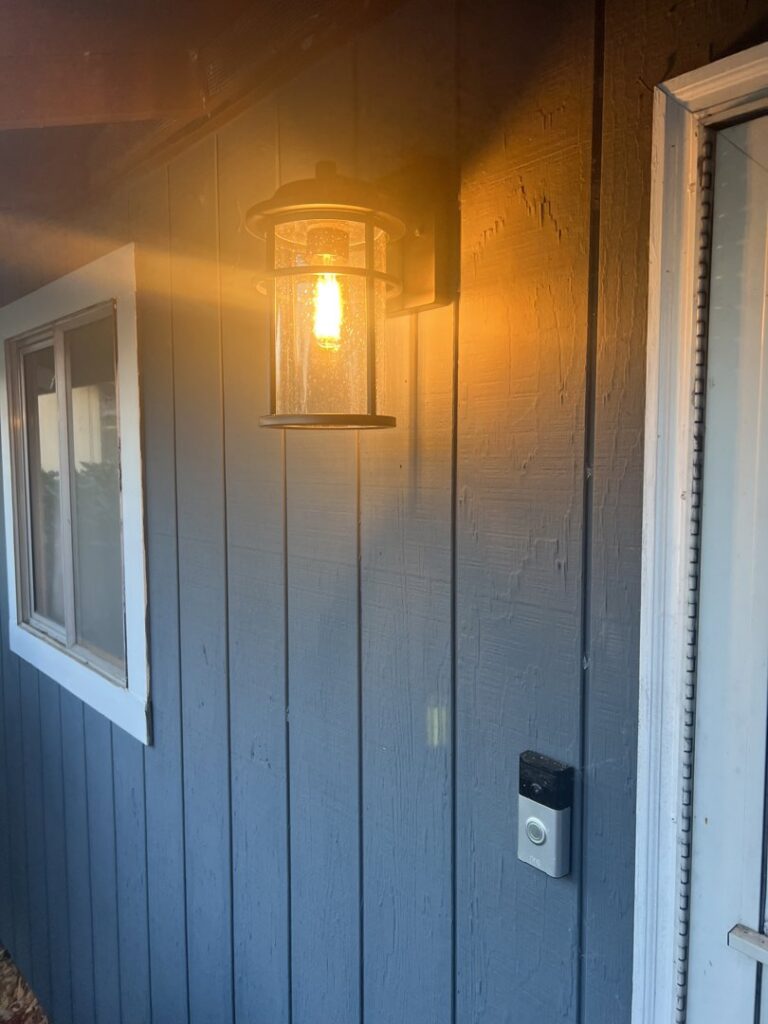 An outdoor wall light fixture installed and illuminated next to a door by Andrew's Electric in Kent, WA