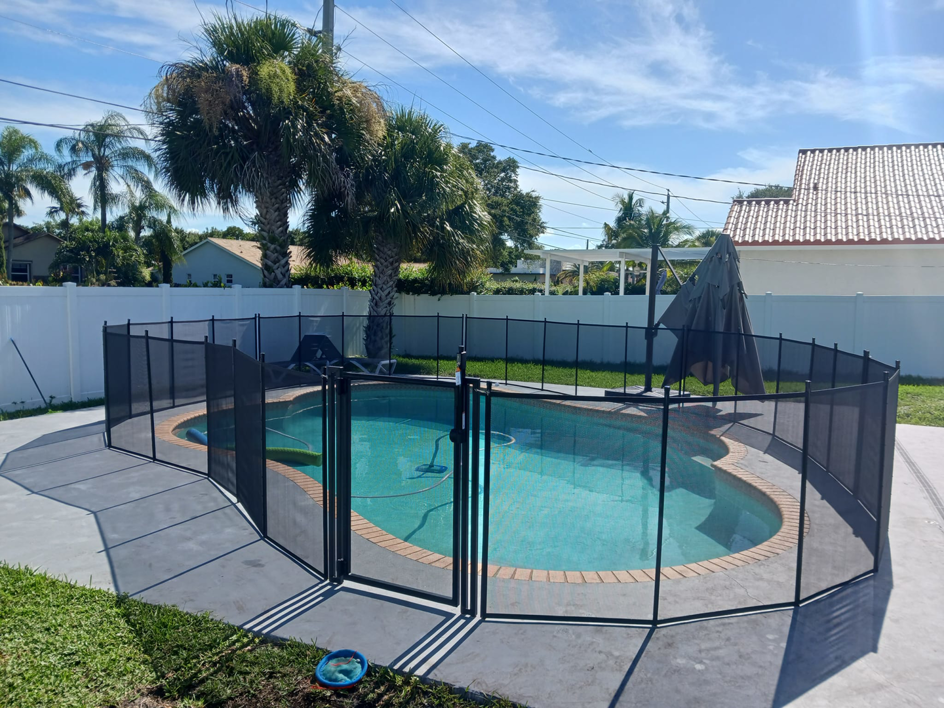 An oval swimming pool secured with a black mesh safety fence by All Brand Pool Fence in Fort Lauderdale, FL.