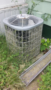 An outdoor air conditioning unit overgrown with grass, requiring maintenance from Cheaper Plumbing & Heating in Lansing, MI