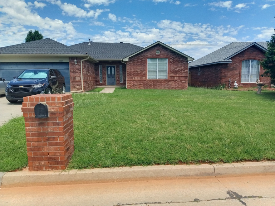 An overgrown front lawn of a brick house, ready for professional mowing by You're Choice Lawn Care LLC in Oklahoma City, OK.