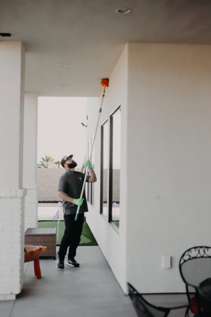 A Pallas Pest Control employee removing spider webs from a high corner of a building in Saint George, UT.