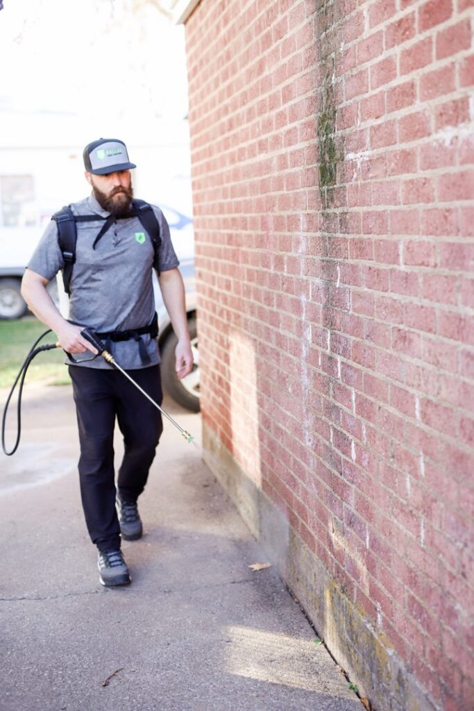 A Pallas Pest Control technician spraying along a brick wall for pest treatment in Saint George, UT.