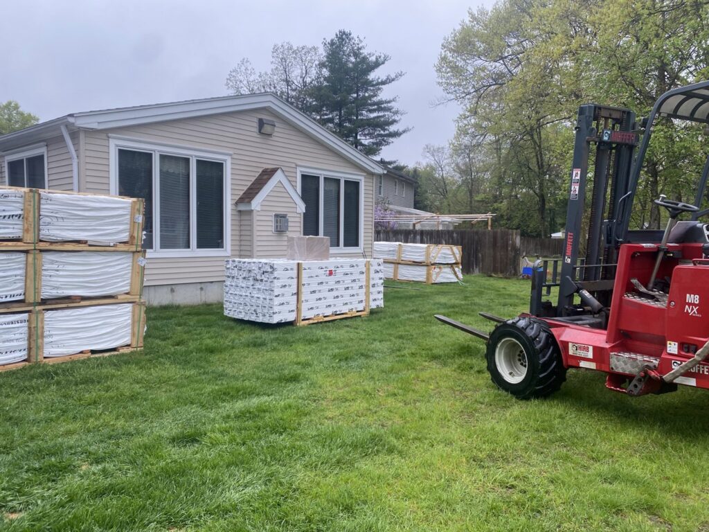 Pallets of vinyl fencing materials and a forklift on a job site for Texeira Fencing & Concrete in Springfield, MA.
