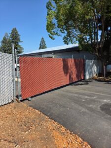 A chain-link fence with red privacy slats and a sliding gate installed by Palmers Iron Fence in Sacramento, CA.