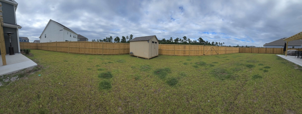 A panoramic view of a large backyard with a new wood fence installed by Montiel Fence Works in Wilmington, NC.