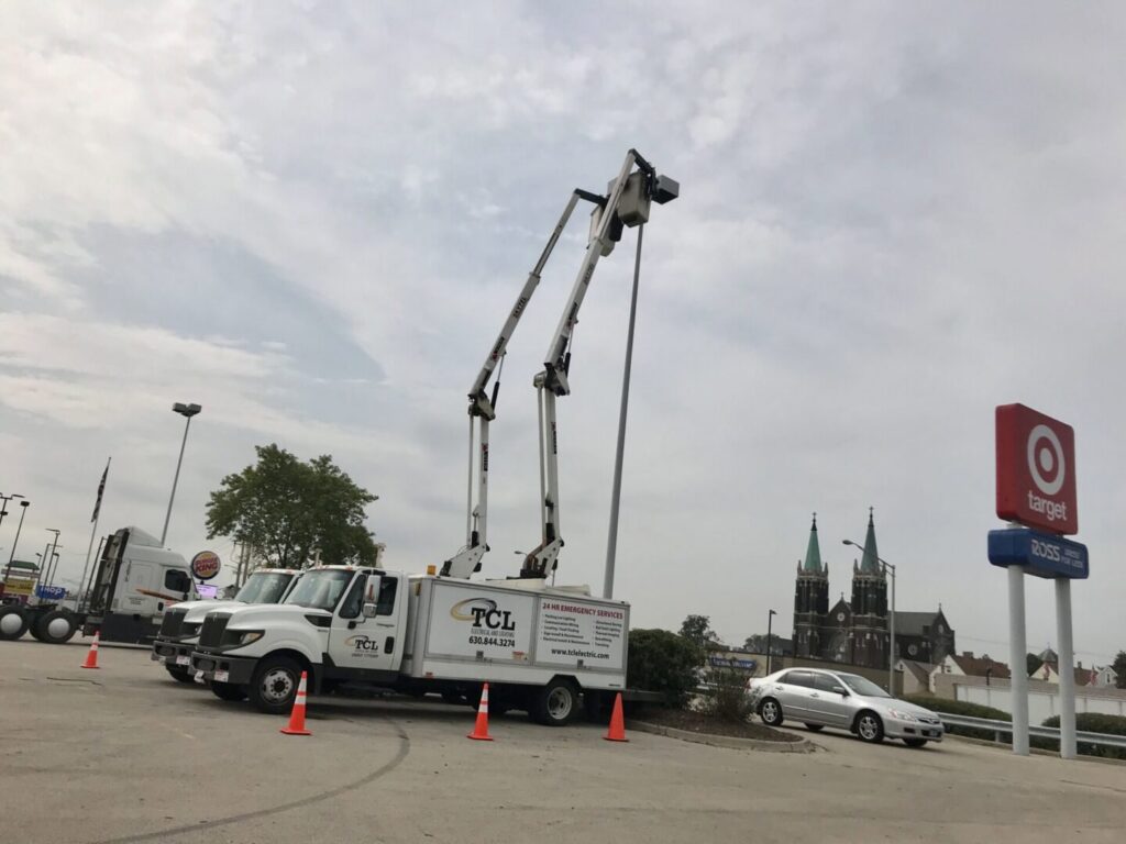 TCL Electrical and Lighting team performing parking lot lighting maintenance with two boom trucks in North Aurora, IL