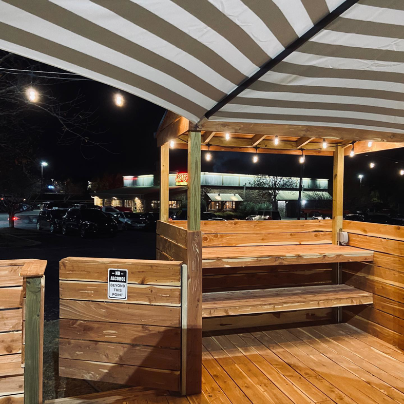Patio string lights illuminating a wooden outdoor seating area, installed by Natural State Electric LLC in Fayetteville, AR.
