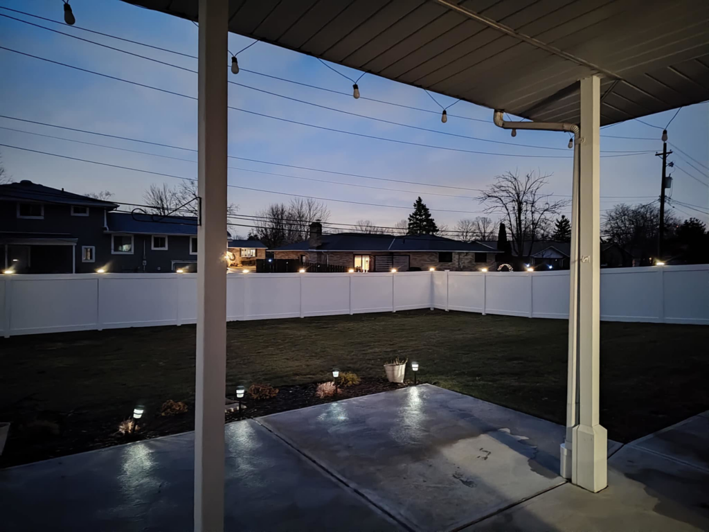 View from a patio showing a newly installed white vinyl fence with post lights by Fence Guys INC in Cleveland, OH.