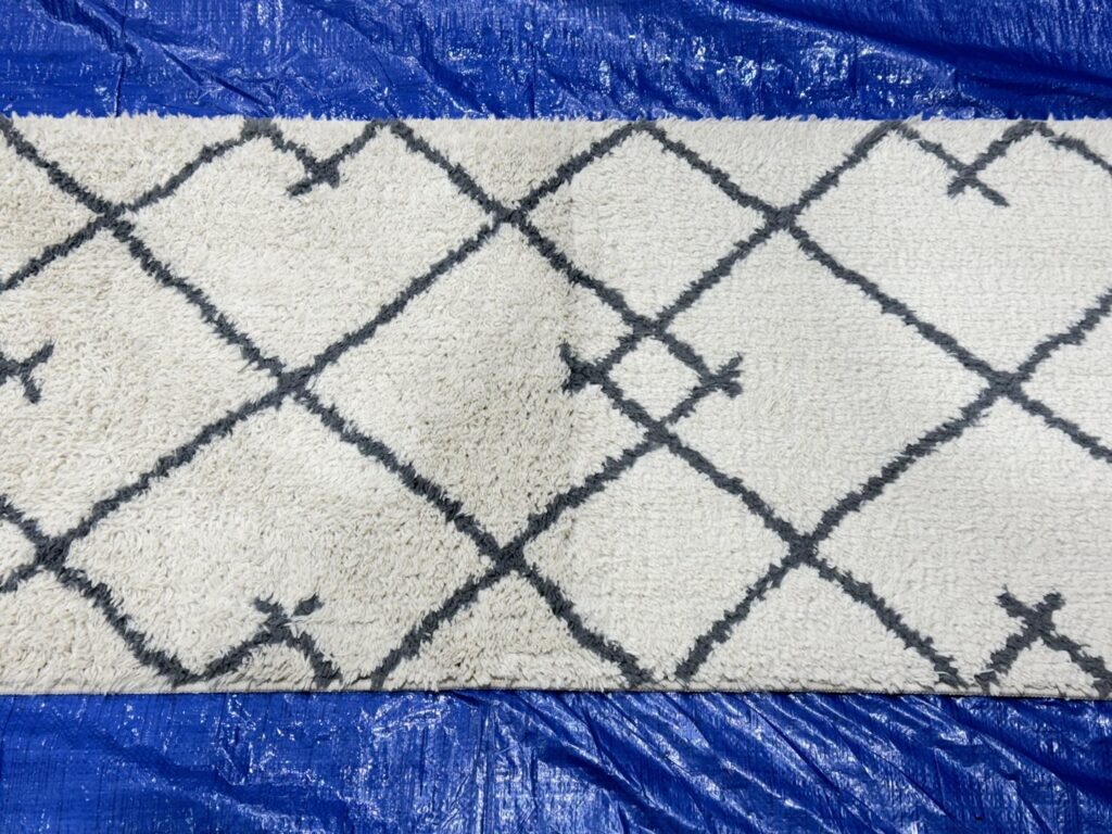 A white and grey patterned area rug laid on a blue tarp, undergoing professional cleaning by Strictly Tile & Carpet Care in Lansing, MI.